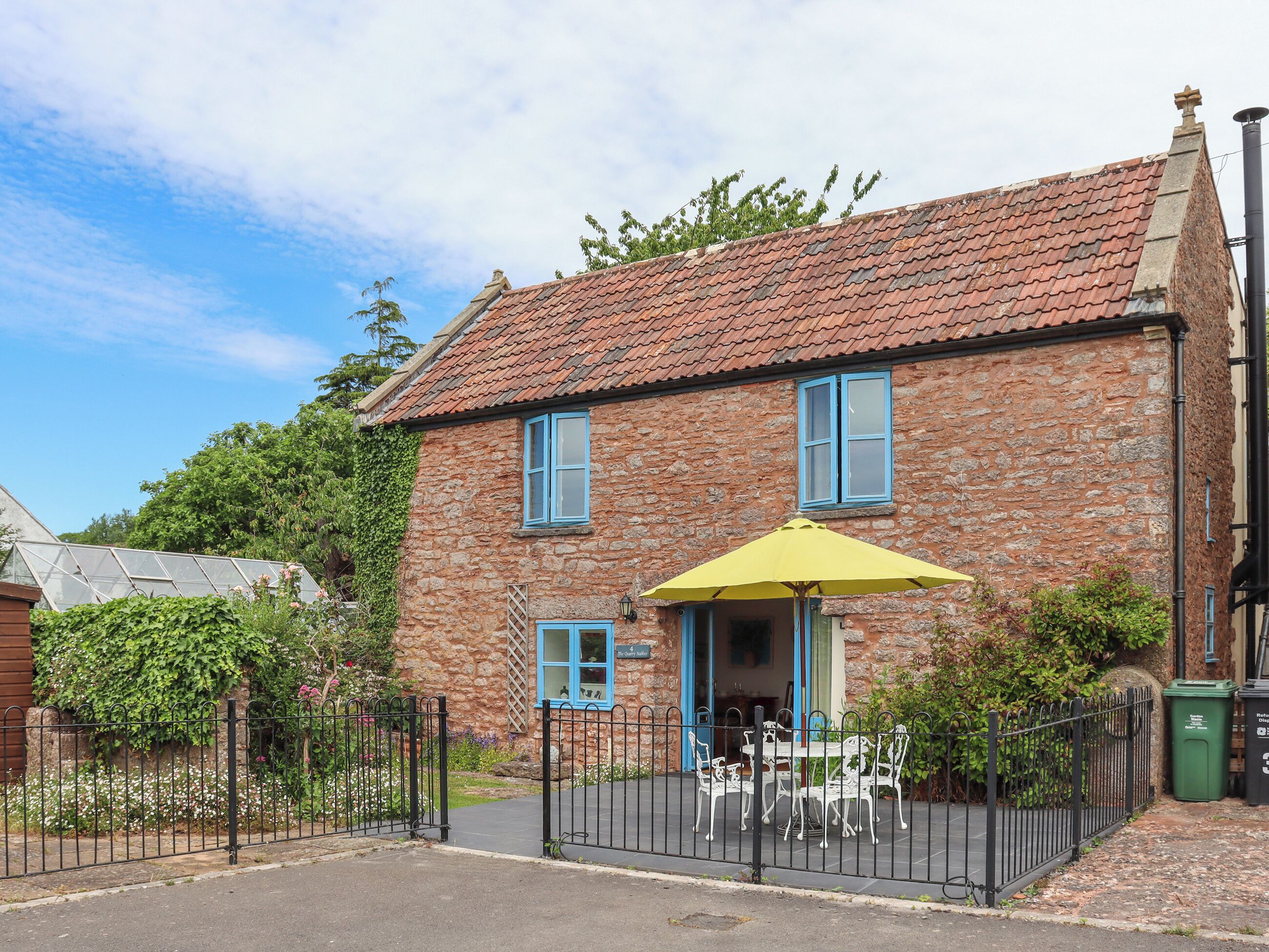 A stone building with a tiled roof, a gated entrance, and a patio with outdoor furniture.