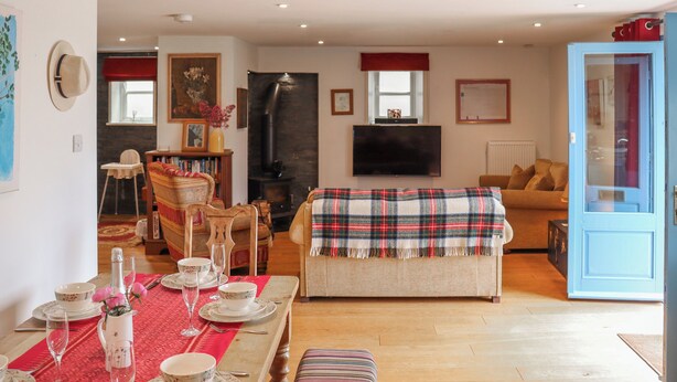 A living room with a sofa, a dining table set for a meal, a television, and a fireplace. - 3 bedroom accommodation in Cheddar (Cheddar)