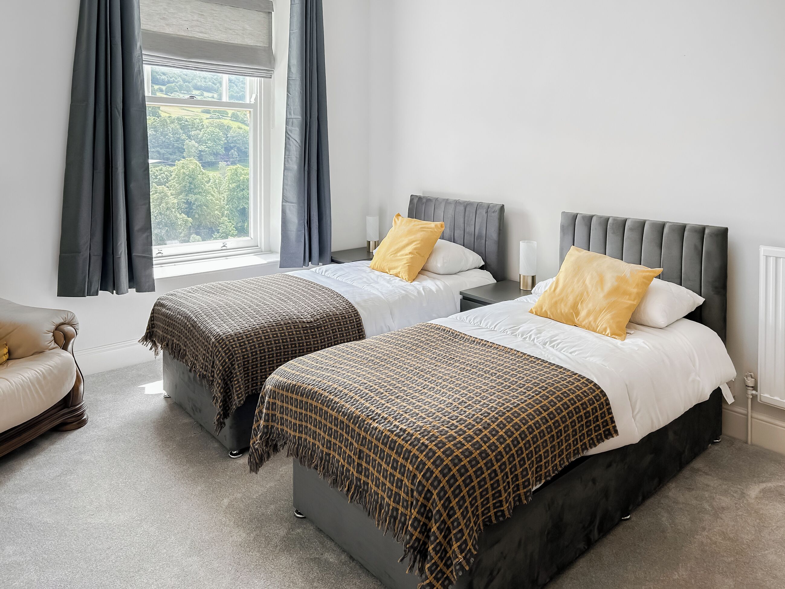A hotel room with two beds, a sofa, and a window with curtains.