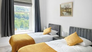 Een hotelkamer met twee bedden, een raam met gordijnen, een nachtkastje met een lamp en een schilderij aan de muur.