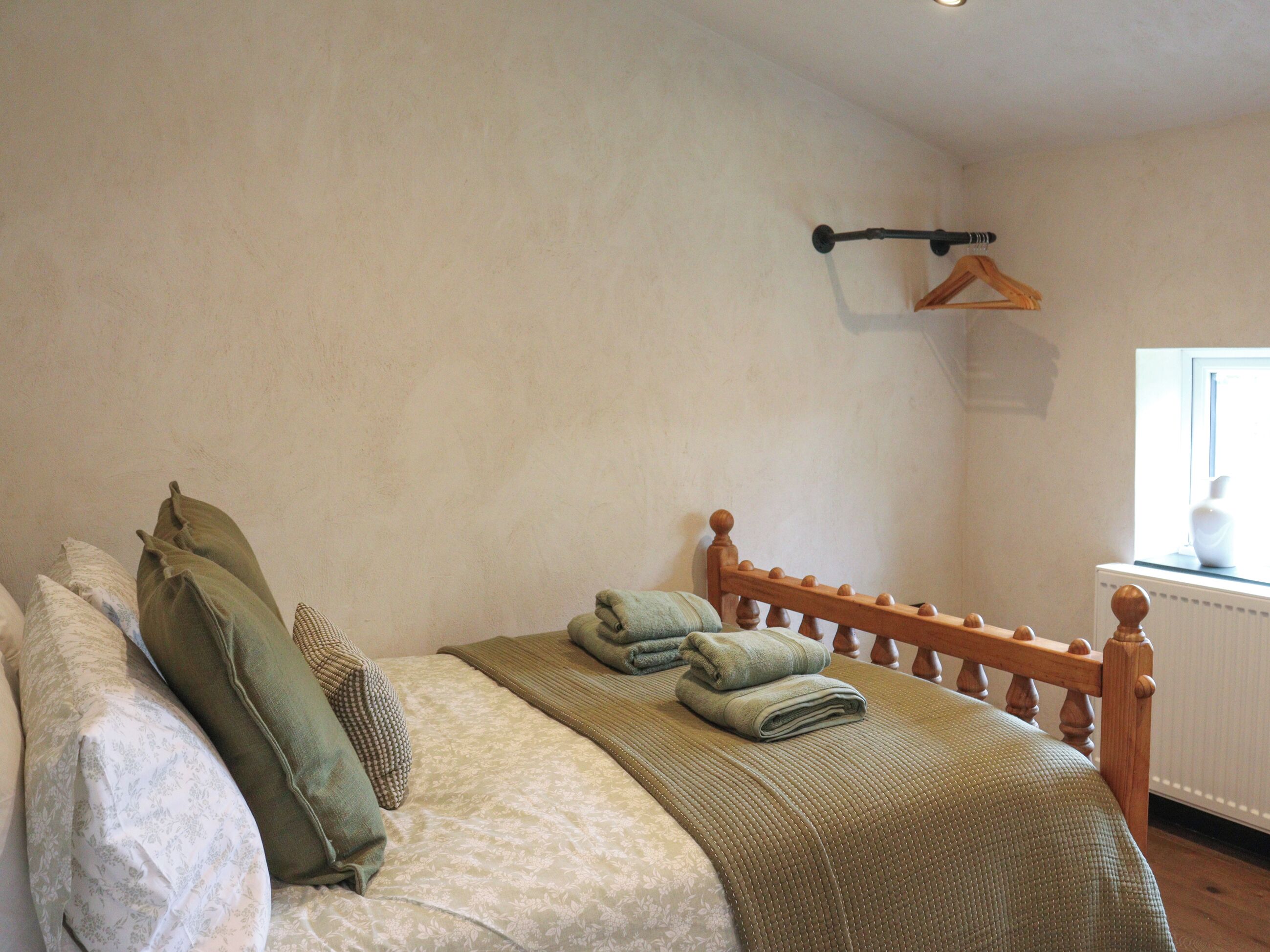 A bedroom with a bed, pillows, a hanging coat rack, and a window.