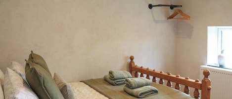A bedroom with a bed, pillows, a hanging coat rack, and a window.