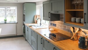 Een keuken met grijze kastjes, een houten aanrechtblad, een inbouwoven en een raam met uitzicht.