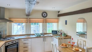 A modern kitchen with a gas stove, oven, and microwave. There is a dining table with chairs and a window with curtains. - 2 bedroom accommodation in Barnard Castle (Barnard Castle)
