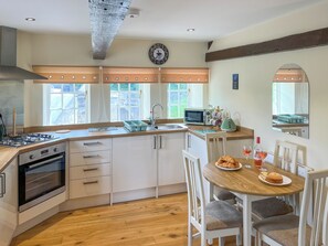 A modern kitchen with a gas stove, oven, and microwave. There is a dining table with chairs and a window with curtains.