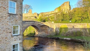 A stone bridge over a river, a stone building with windows, and a castle in the background. - 2 bedroom accommodation in Barnard Castle (Barnard Castle)