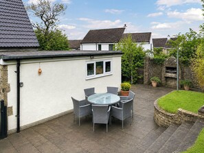 A patio with a round table and chairs, a stone wall, and a brick oven. - 4 bedroom accommodation in Addingham, near Ilkley (Addingham, near Ilkley)