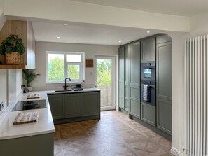 A modern kitchen with a central island, built-in appliances, and a view of greenery outside. - 4 bedroom accommodation in Addingham, near Ilkley (Addingham, near Ilkley)