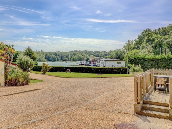 A gravel driveway leading to a wooden deck with a view of a lake, boats, and a row of cabins.