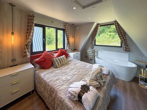 A bedroom with a large bed, a built-in bathtub, and a window with curtains. - 2 bedroom accommodation in Pen-Y-Felin, near Mold (Pen-Y-Felin, near Mold)