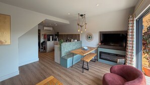 Uma sala de estar moderna com uma mesa de centro de madeira, uma cadeira vermelha, um sofá cinza, uma mesa de jantar e uma TV na parede.