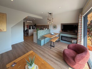 A modern living room with a wooden coffee table, a red chair, a grey sofa, a dining table, and a TV mounted on the wall. - 2 bedroom accommodation in Pen-Y-Felin, near Mold (Pen-Y-Felin, near Mold)