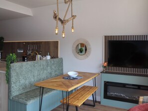 A modern kitchen with a built-in oven, a dining area with a bench, and a TV mounted on the wall. - 2 bedroom accommodation in Pen-Y-Felin, near Mold (Pen-Y-Felin, near Mold)