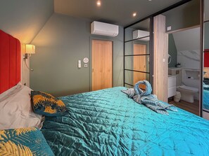 A bedroom with a bed, a red headboard, a wall-mounted air conditioner, a wooden door, and a bathroom visible through a glass partition. - 2 bedroom accommodation in Pen-Y-Felin, near Mold (Pen-Y-Felin, near Mold)