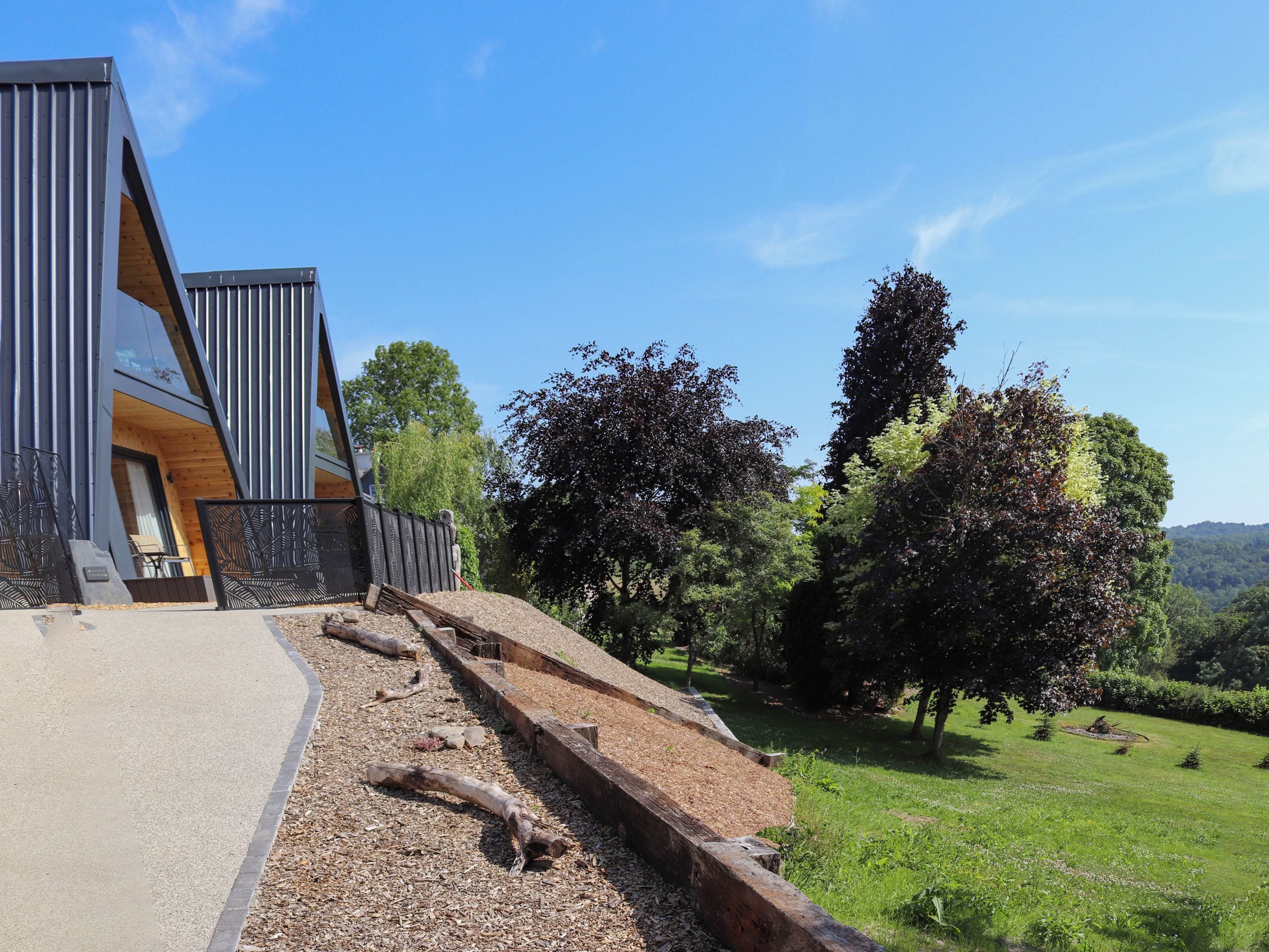 A modern building with a sloped roof, a wooden deck, and a paved area with a wooden bench.