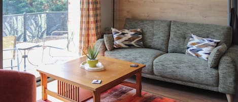 Una sala de estar con sofá, una mesa de centro con una planta, un tapete estampado y vistas al exterior.