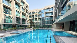 En modern byggnad med flera våningar, stora fönster och en central pool omgiven av solstolar.
