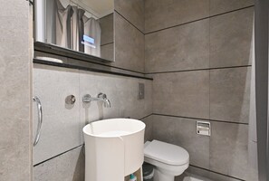 A modern bathroom with a white sink, a toilet, and a mirror above the sink. - Bloomfields Studio in Signature Living South - JVC (Jumeirah Village Circle)