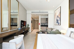 A modern hotel room with a large bed, a TV, a desk with a computer, and a kitchenette in the background. - Bloomfields Studio in Signature Living South - JVC (Jumeirah Village Circle)