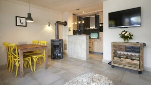 A modern kitchen with a TV, wooden dining table, yellow chairs, and a wine cooler cart. - Apartment mit Strandkorb in Ückeritz (Seebad Ueckeritz)
