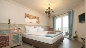 Un dormitori amb un llit, una làmpada penjant, una televisió, una finestra amb cortines i un moble decoratiu.