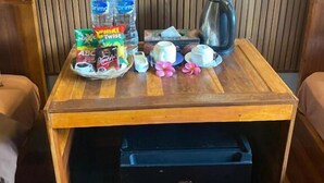A wooden table with a GEA refrigerator, two bottles of water, a coffee pot, a plate with snacks, and a small decorative item.