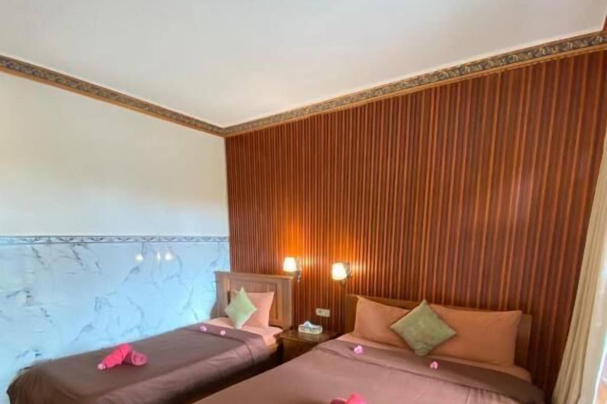 Habitación de hotel con dos camas, piso de baldosas de mármol, paneles de madera en la pared y una mesita de noche con lámpara.