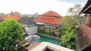 A rooftop pool with a view of traditional buildings, a covered seating area, and a stone wall.