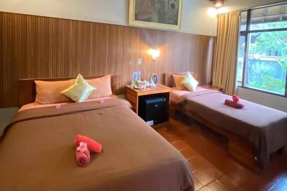 Habitación de hotel con dos camas, una mesita de noche, una ventana con cortinas y un cuadro en la pared.