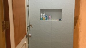 Un petit espace douche fermé, comprenant des toilettes, une pomme de douche et une étagère pour les articles de toilette.