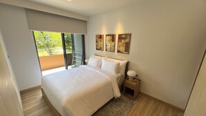 A modern hotel room with a large bed, a nightstand, a lamp, and a balcony with a view of greenery. - Skypark Celeste Laguna Residences - WSYY (Choeng Thale)