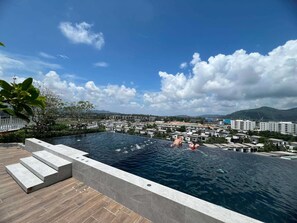 A swimming pool with steps leading into it, surrounded by a cityscape and mountains in the background. - Skypark Celeste Laguna Residences - WSYY (Choeng Thale)
