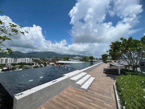 A swimming pool with a wooden deck and a view of a cityscape and mountains. - Skypark Celeste Laguna Residences - WSYY (Choeng Thale)