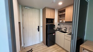 A compact kitchen with a microwave, refrigerator, sink, and wooden cabinets. - Skypark Celeste Laguna Residences - WSYY (Choeng Thale)