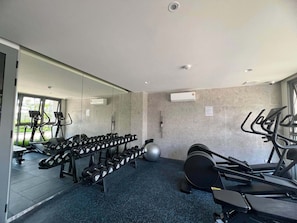 A gym with exercise equipment, a mirrored wall, and a window. - Skypark Celeste Laguna Residences - WSYY (Choeng Thale)