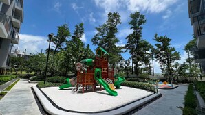 A playground with slides and climbing structures surrounded by trees and a clear sky. - Skypark Celeste Laguna Residences - WSYY (Choeng Thale)