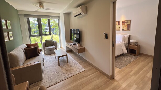 A modern hotel room with a sofa, armchair, TV, and a bed. - Skypark Celeste Laguna Residences - WSYY (Choeng Thale)