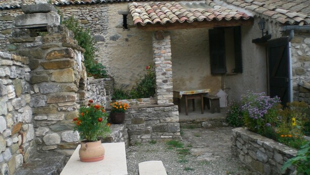 A stone building with a tiled roof, a small table, and potted plants. - Les Pierres Séches Vacation Rental, Les Andrieux 4/5 Banon (Banon)