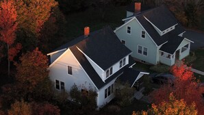 A two-story house with a dark roof, surrounded by trees with autumn foliage.
