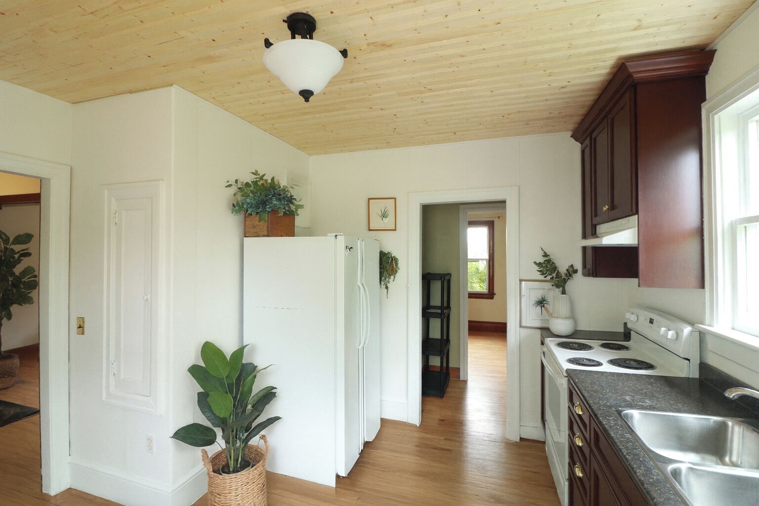 Una cocina con pisos de madera, gabinetes blancos, un refrigerador, una estufa y una lámpara en el techo.