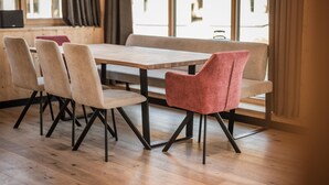 A dining area with a wooden table and four chairs, one with a red cushion, in a room with large windows and wooden floors. - Bichlbach Chalet With Sauna (Bichlbach)
