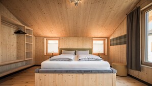 A wooden-paneled bedroom with a bed, two bedside tables, a hanging light fixture, and a window with curtains. - Bichlbach Chalet With Sauna (Bichlbach)
