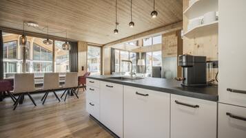 A modern kitchen with wooden cabinets, a black coffee machine, and a large window overlooking a mountainous landscape.