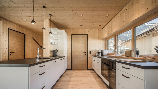 A modern kitchen with wooden walls, white cabinets, and a central island. - Bichlbach Chalet With Sauna (Bichlbach)