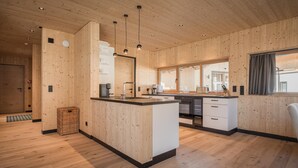 A modern kitchen with wooden paneling, a central island, pendant lighting, and a view through a large window. - Bichlbach Chalet With Sauna (Bichlbach)