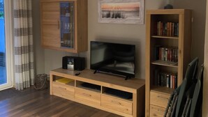 A living room with a flat-screen TV, wooden cabinets, a bookshelf, and a painting on the wall.