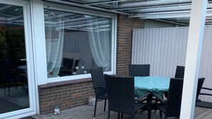 A covered patio with a table and chairs, a glass door, and a brick wall.