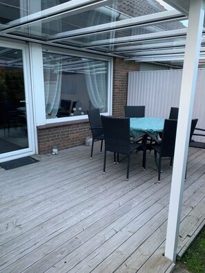Eine überdachte Terrasse mit Tisch, Stühlen, einer Glastür und einer Backsteinmauer.