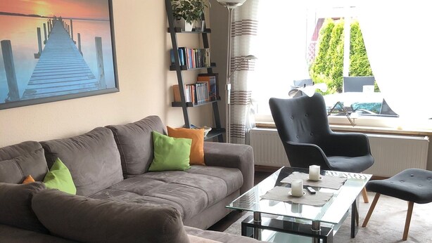 A living room with a sofa, a glass coffee table, a bookshelf, and a view of the outdoors.