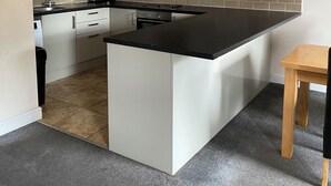 Une cuisine moderne avec un îlot central, des meubles blancs, un plan de travail noir et une petite table en bois.
